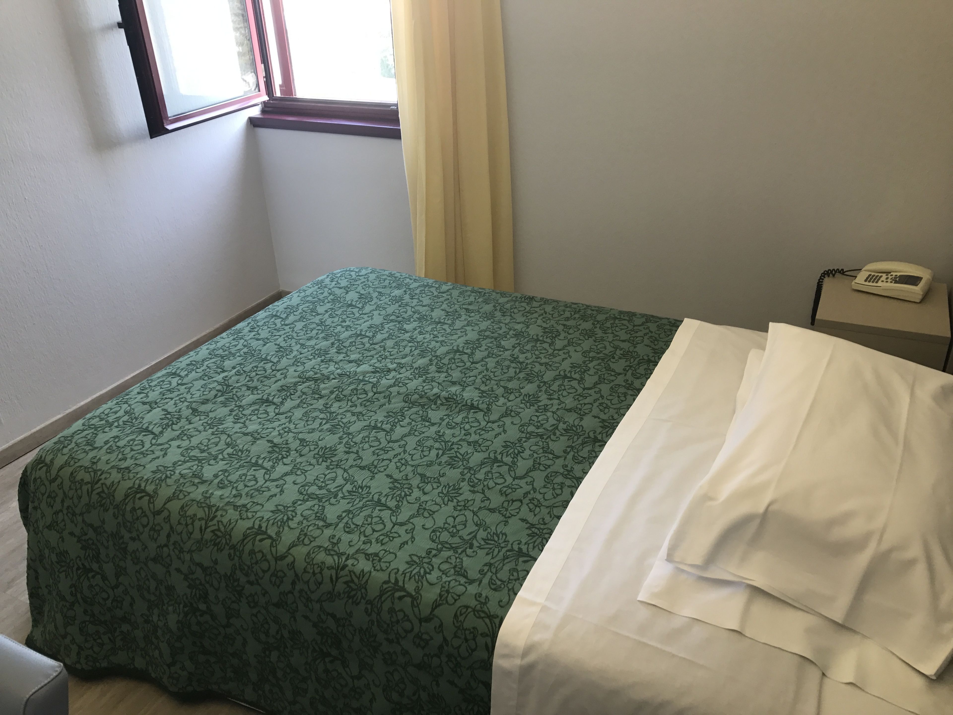 A hotel room with a bed, a window, a telephone, and a curtain.