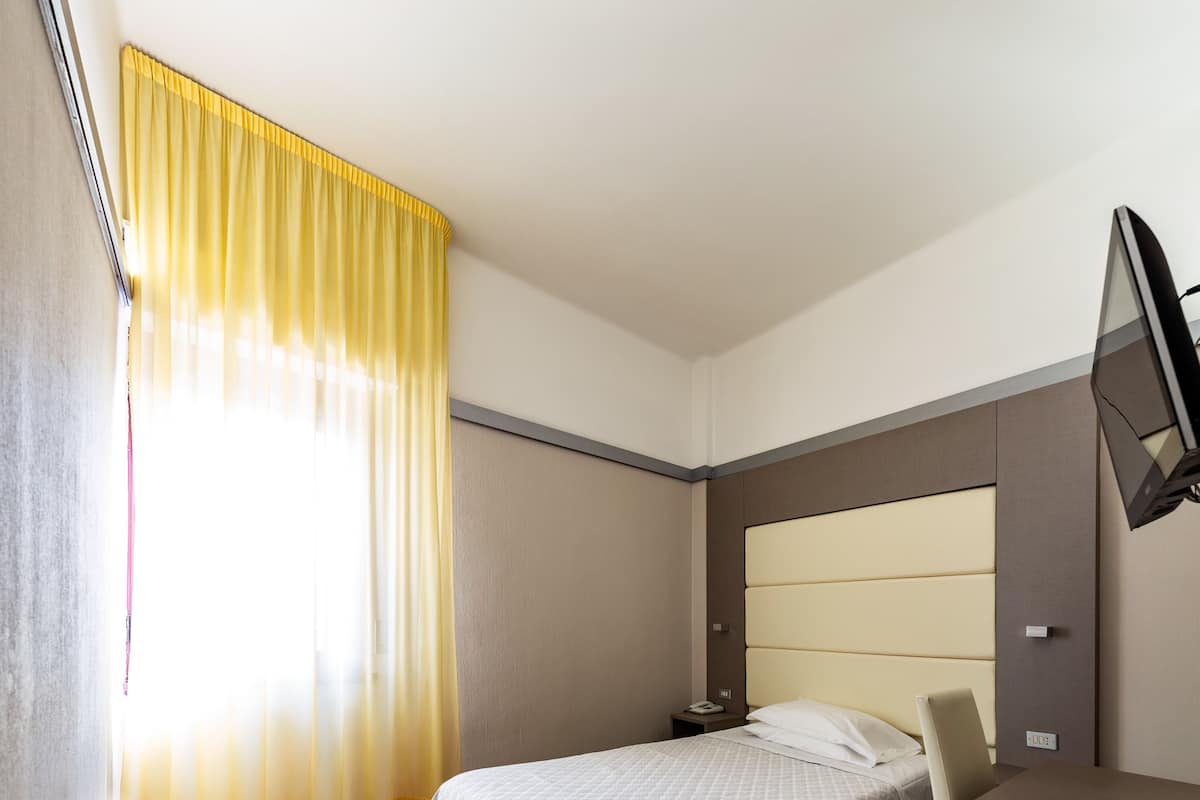 Una habitación de hotel con una cama, mesita de noche y un televisor instalado en la pared.