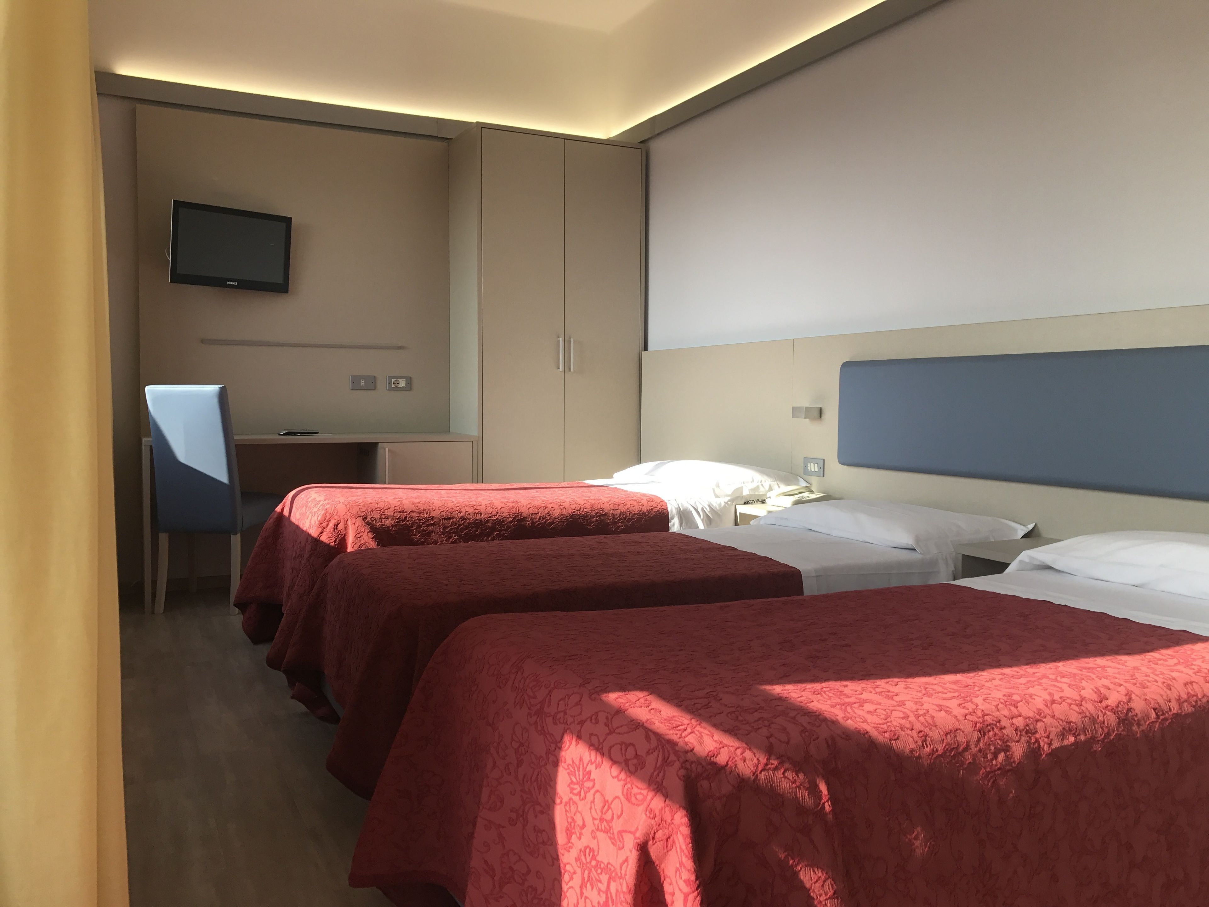 A hotel room with two beds, a desk, a chair, and a TV on the wall.