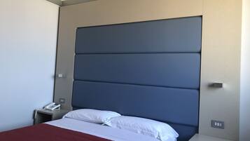 Una camera d'albergo moderna con un letto grande, lenzuola bianche, una coperta rossa e un comodino con il telefono.