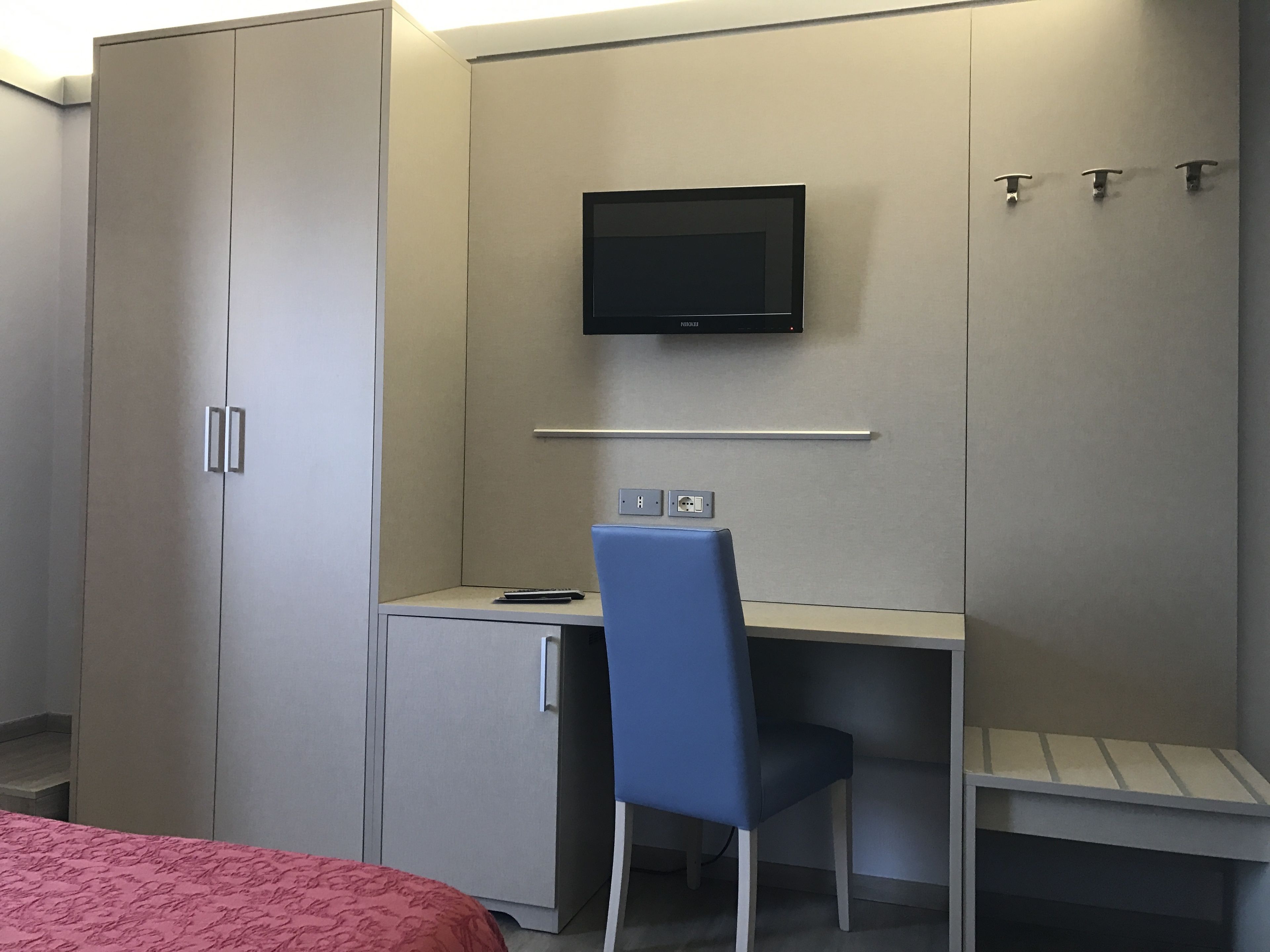 Ein Schlafzimmer mit einem Bett, einem Schreibtisch mit Stuhl, einem an der Wand befestigten Fernseher und einem Kleiderschrank.