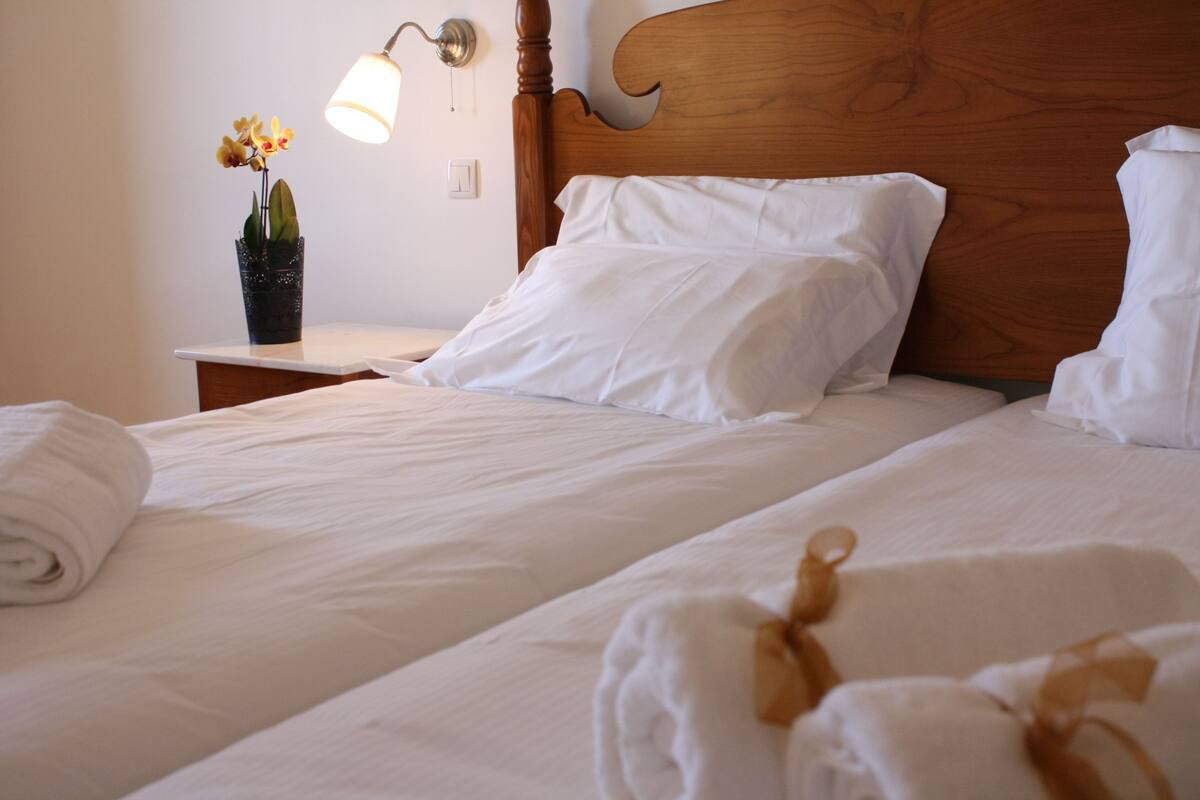 A neatly made bed with white linens and pillows, a wooden headboard, and a small table with a potted orchid.