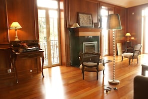 A room with a piano, two chairs, a floor lamp, and a fireplace.
