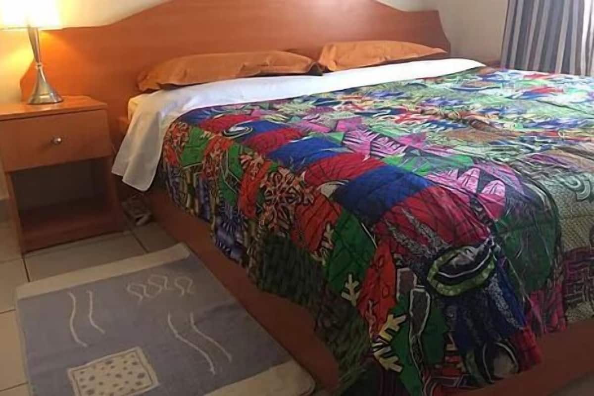 A bed with a colorful quilt, a bedside lamp, and a patterned rug.
