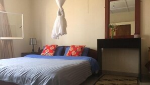 Une chambre à coucher avec un lit, une table de chevet, un miroir et une fenêtre avec des rideaux.