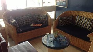 Une pièce comprenant deux canapés en osier ornés de coussins à motifs, une petite table basse en bois avec un vase, et un fauteuil.