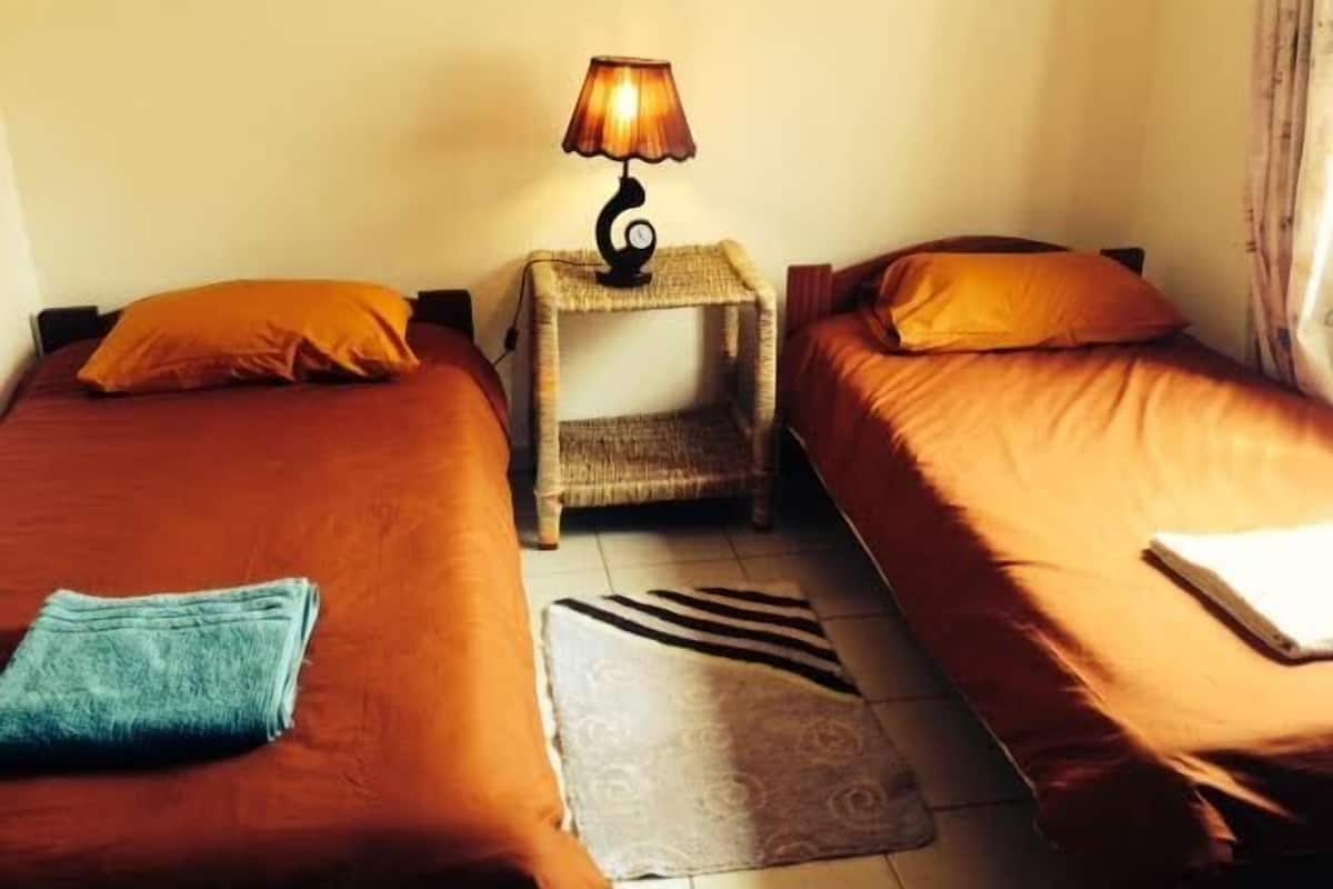 A hotel room with two beds, a nightstand with a lamp, and a striped rug.