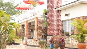 Une maison à deux étages dotée d’un balcon, entourée de plantes en pot et surmontée d’une antenne parabolique.