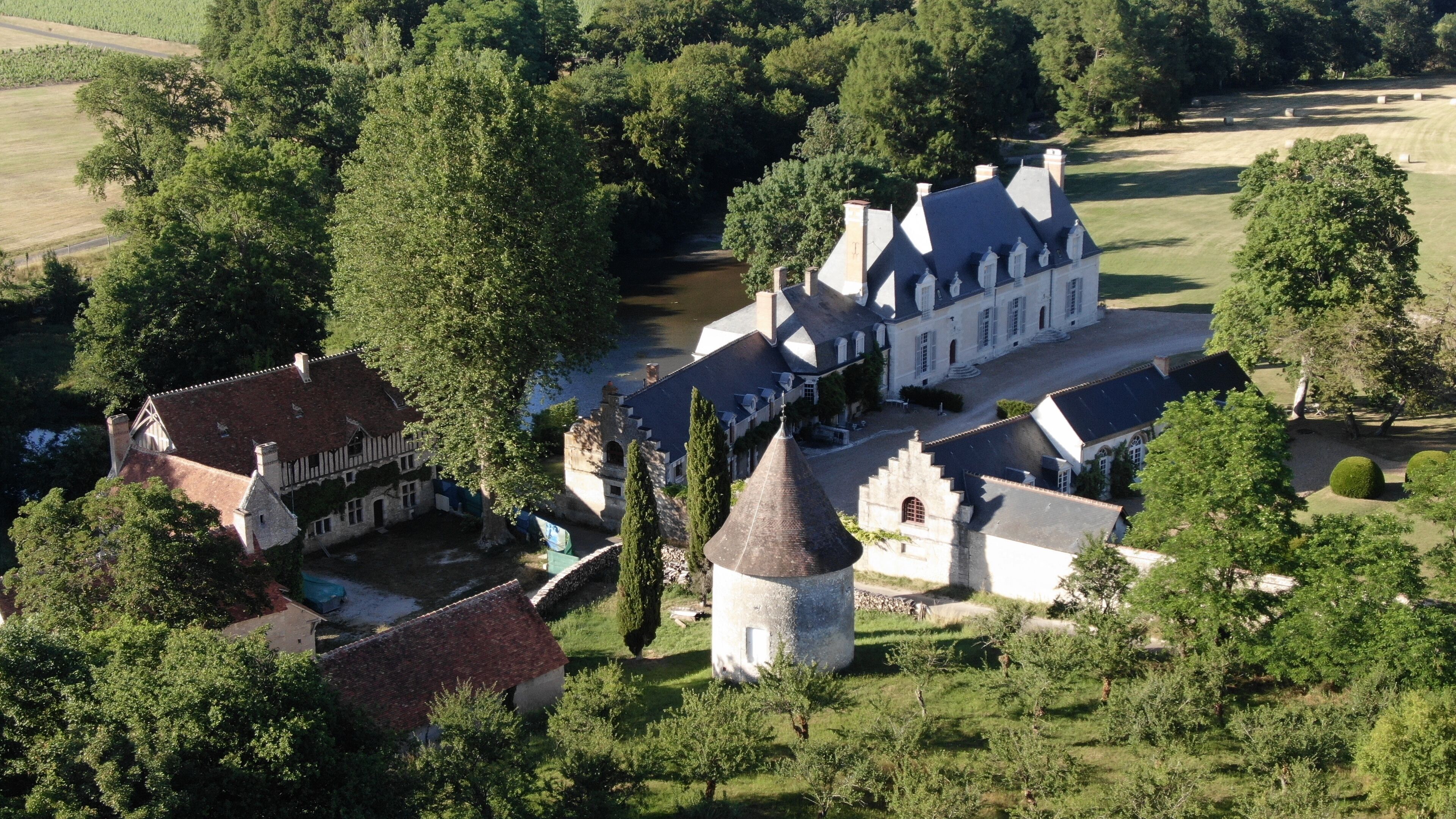 Une vue aérienne d’un domaine historique comprenant plusieurs bâtiments, notamment un grand manoir, une construction plus petite attenante et une tour imposante.