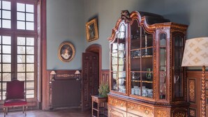 Ein Zimmer mit einem großen Holzkasten, einem roten Sessel, einem Heizkörper und einem Fenster mit vielen Sprossen.