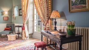 Ein gemütliches Zimmer mit Holzboden, einem rot karierten Sessel, einem Tisch mit Lampe, einem gerahmten Gemälde und einem Fenster mit Vorhängen.
