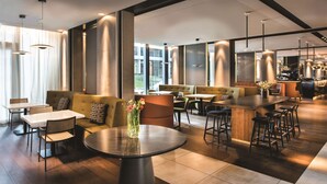 A modern interior with a bar area, seating, and a round table with a vase of flowers. - Adina Apartment Hotel Hamburg Speicherstadt (Hamburg)
