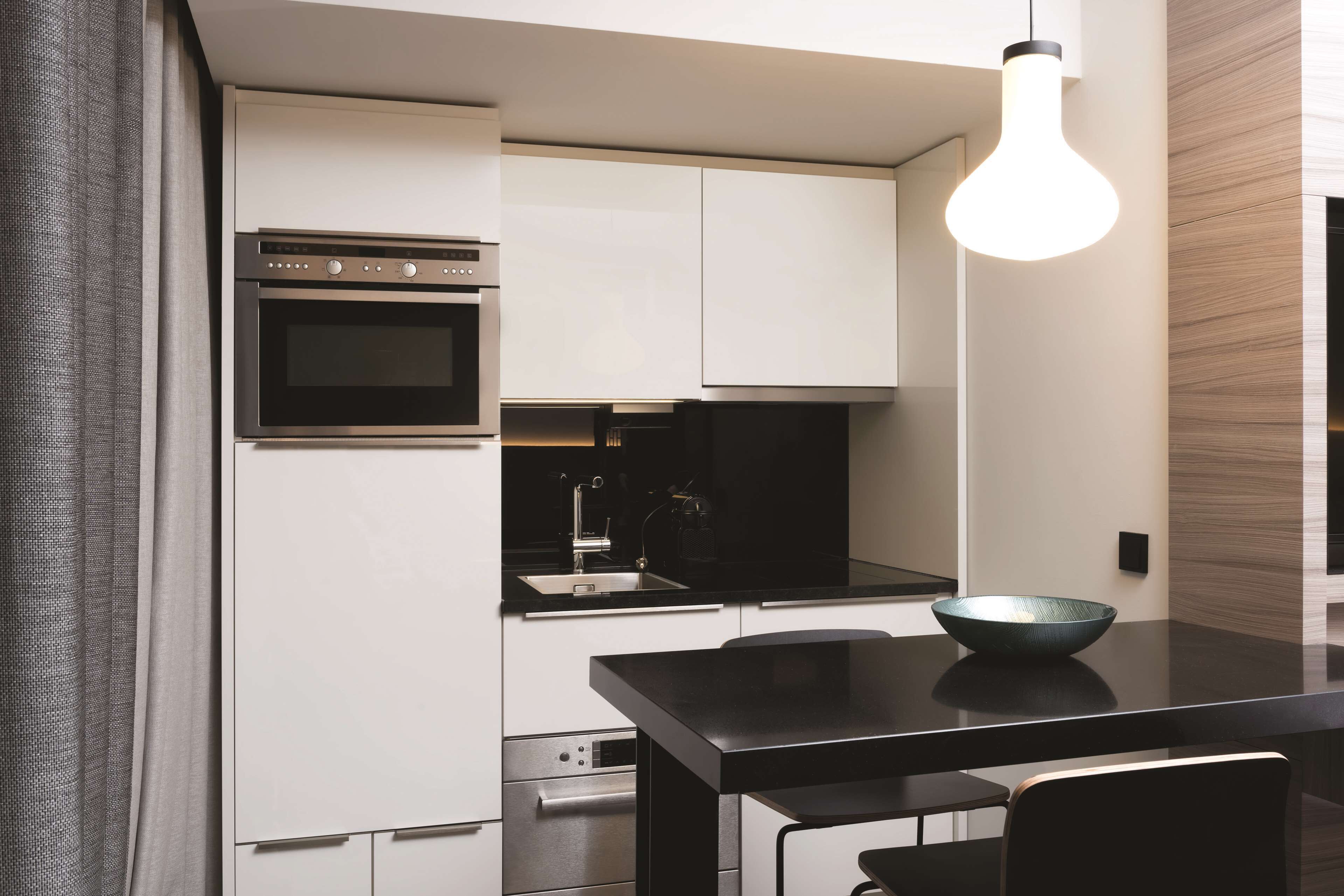 A modern kitchen with white cabinets, a black countertop, and a hanging light fixture.