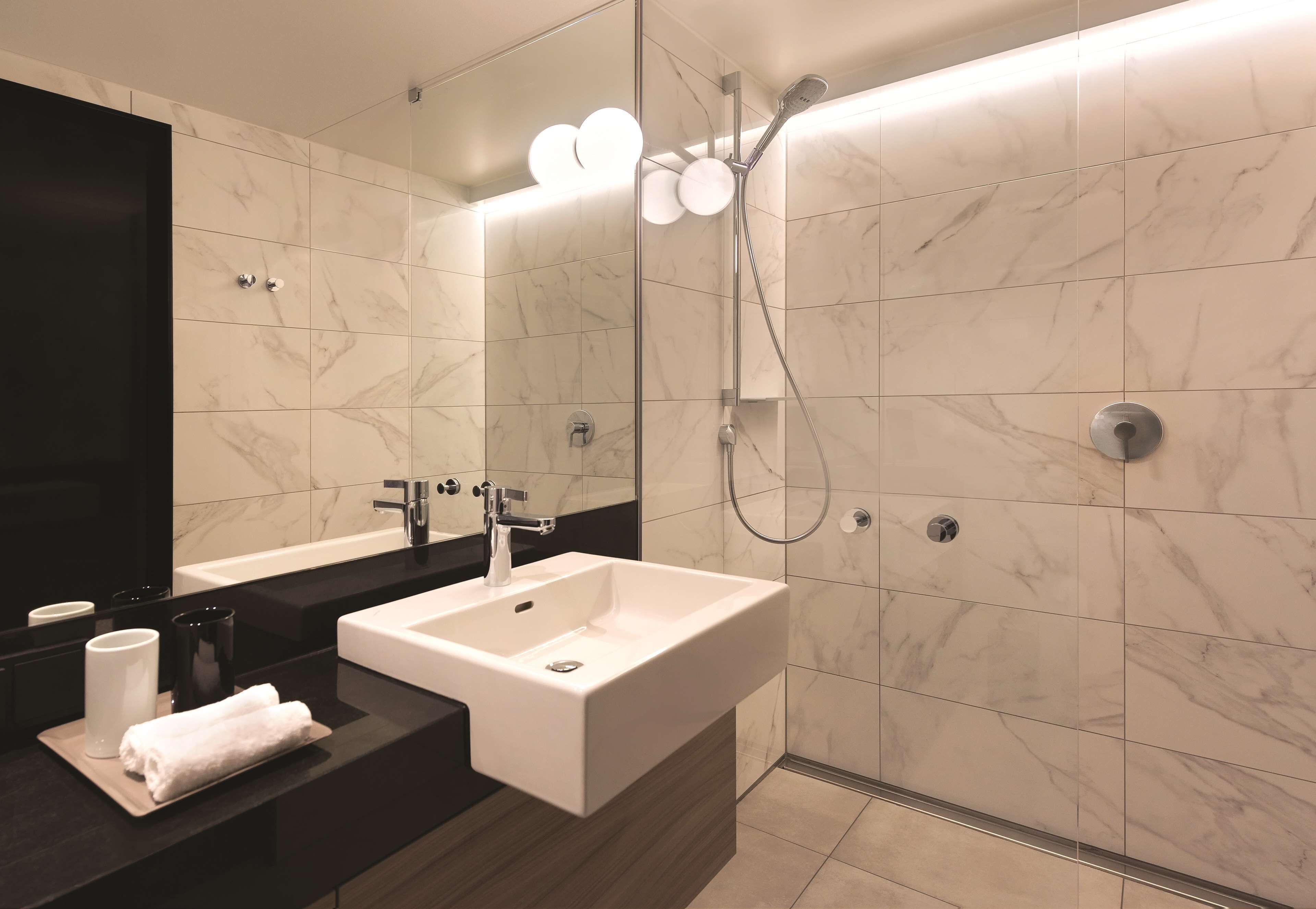 A modern bathroom with a large mirror, a white sink, and a shower area.