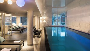 A modern indoor pool area with lounge chairs and a clear view of the cityscape through large windows. - Adina Apartment Hotel Hamburg Speicherstadt (Hamburg)