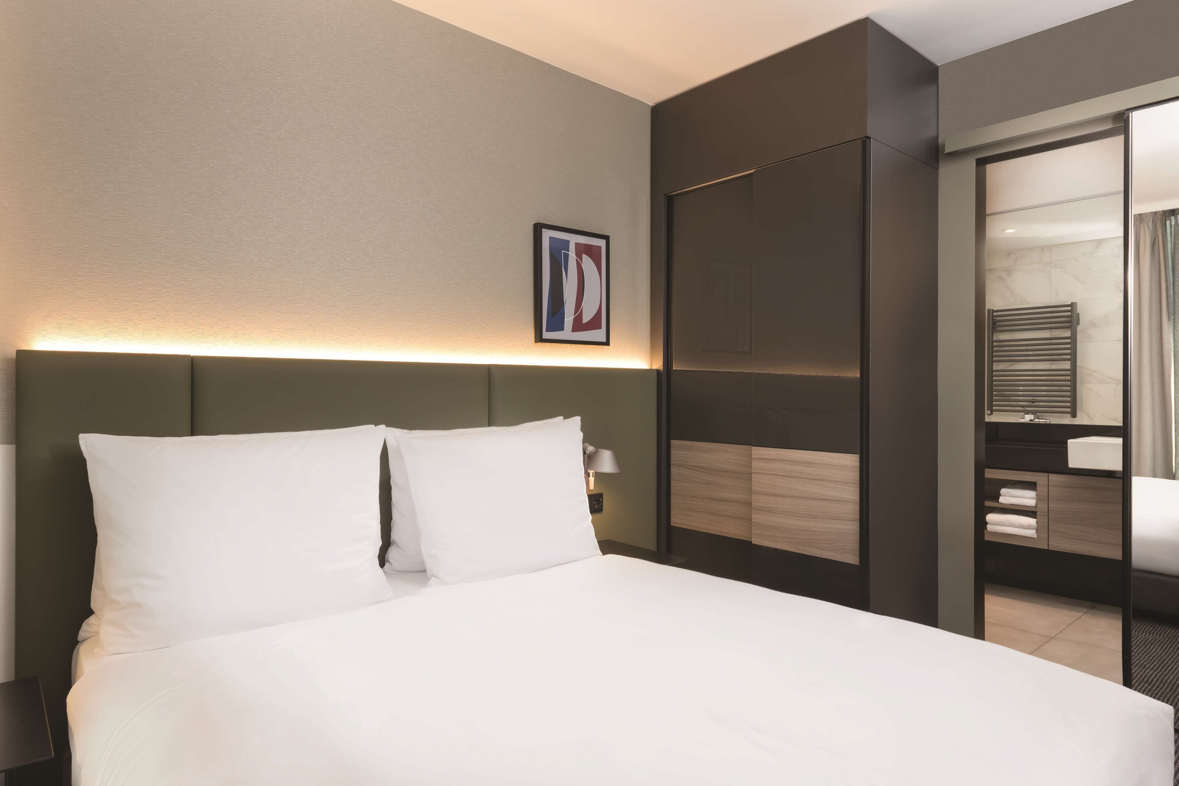 Een moderne hotelkamer met een groot bed, een nachtkastje, een spiegel en een ingelijste foto aan de muur.