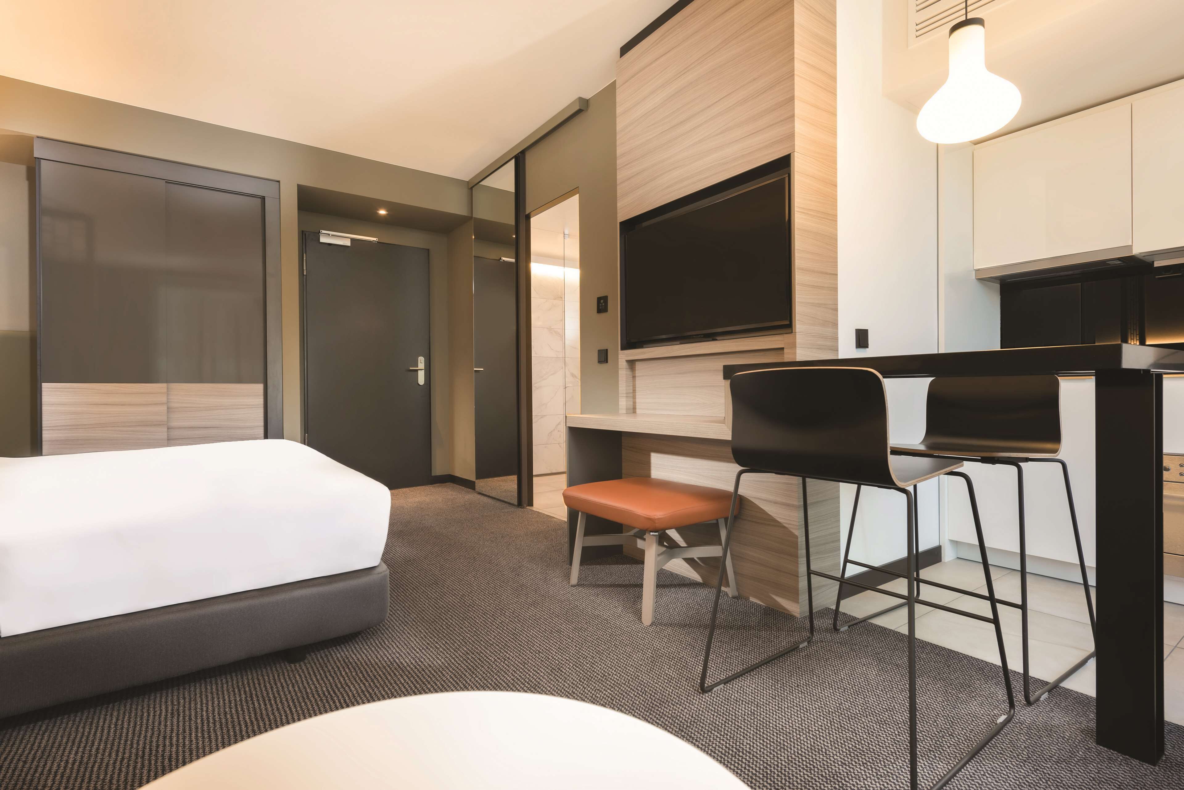 A modern hotel room with a bed, a desk with a chair, a television, and a fireplace.