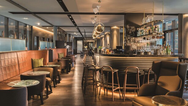 A modern bar area with a curved counter, bar stools, and a variety of bottles and glasses. - Adina Apartment Hotel Hamburg Speicherstadt (Hamburg)