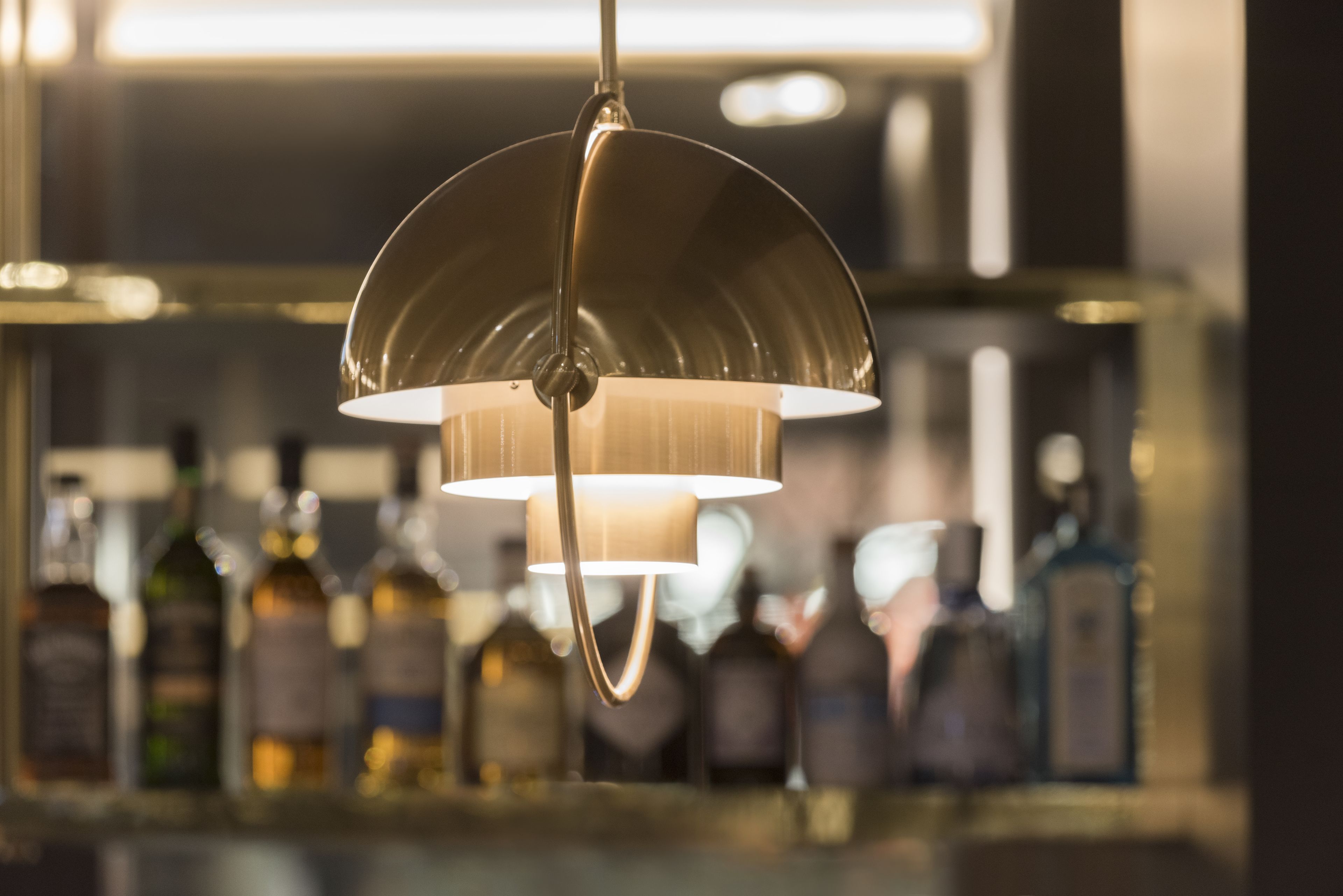 A bar area with a hanging light fixture and bottles in the background.