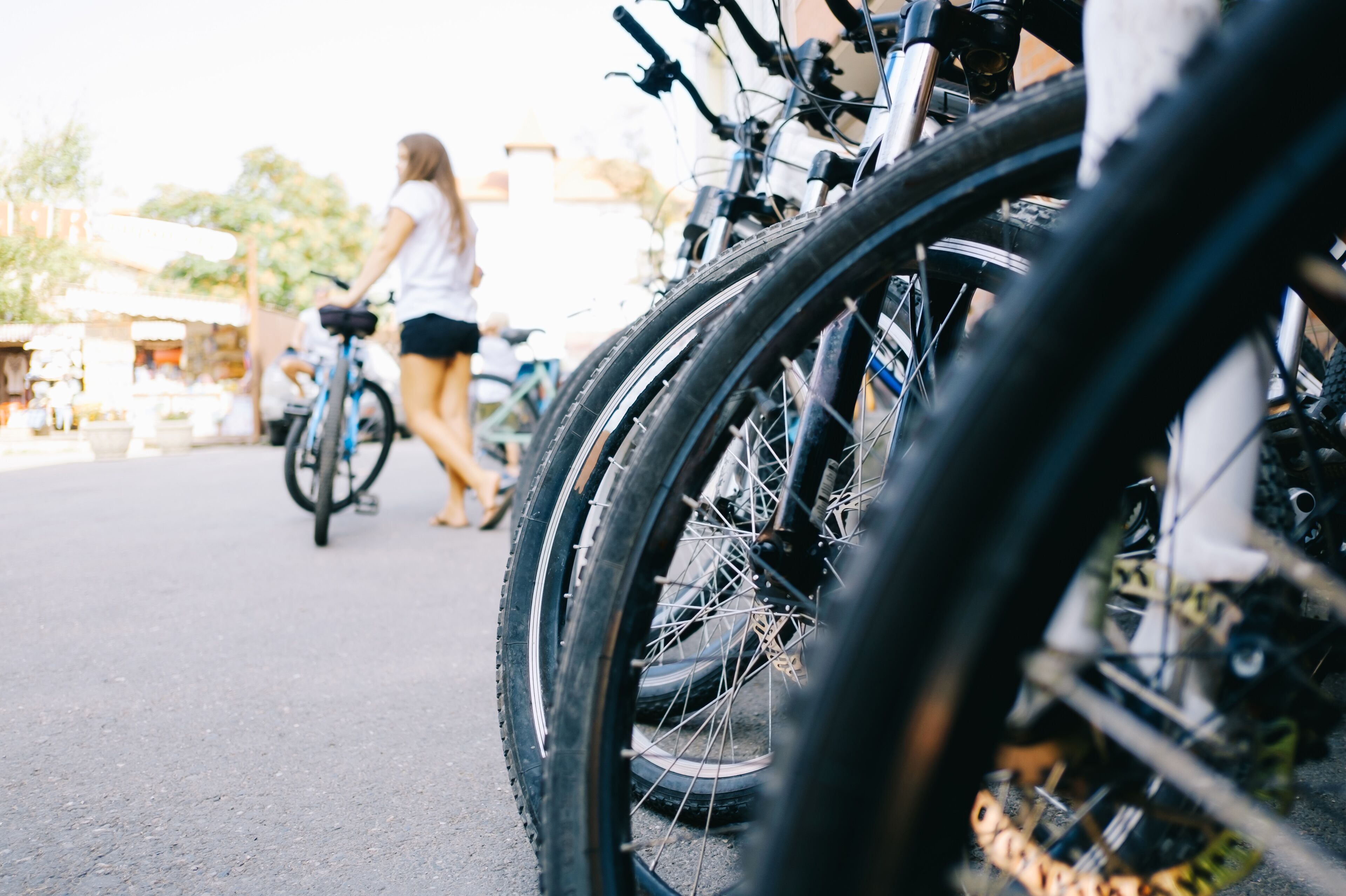 Bicicletas estacionadas en fila, una persona caminando al fondo y un edificio con un letrero.