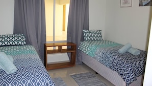 A bedroom with two beds, grey curtains, a wooden nightstand, and a view of a hallway. - Eagle Views Windhoek (Windhoek)