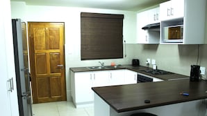 A compact kitchen with white cabinets, a wooden door, a microwave, and a stove. - Eagle Views Windhoek (Windhoek)