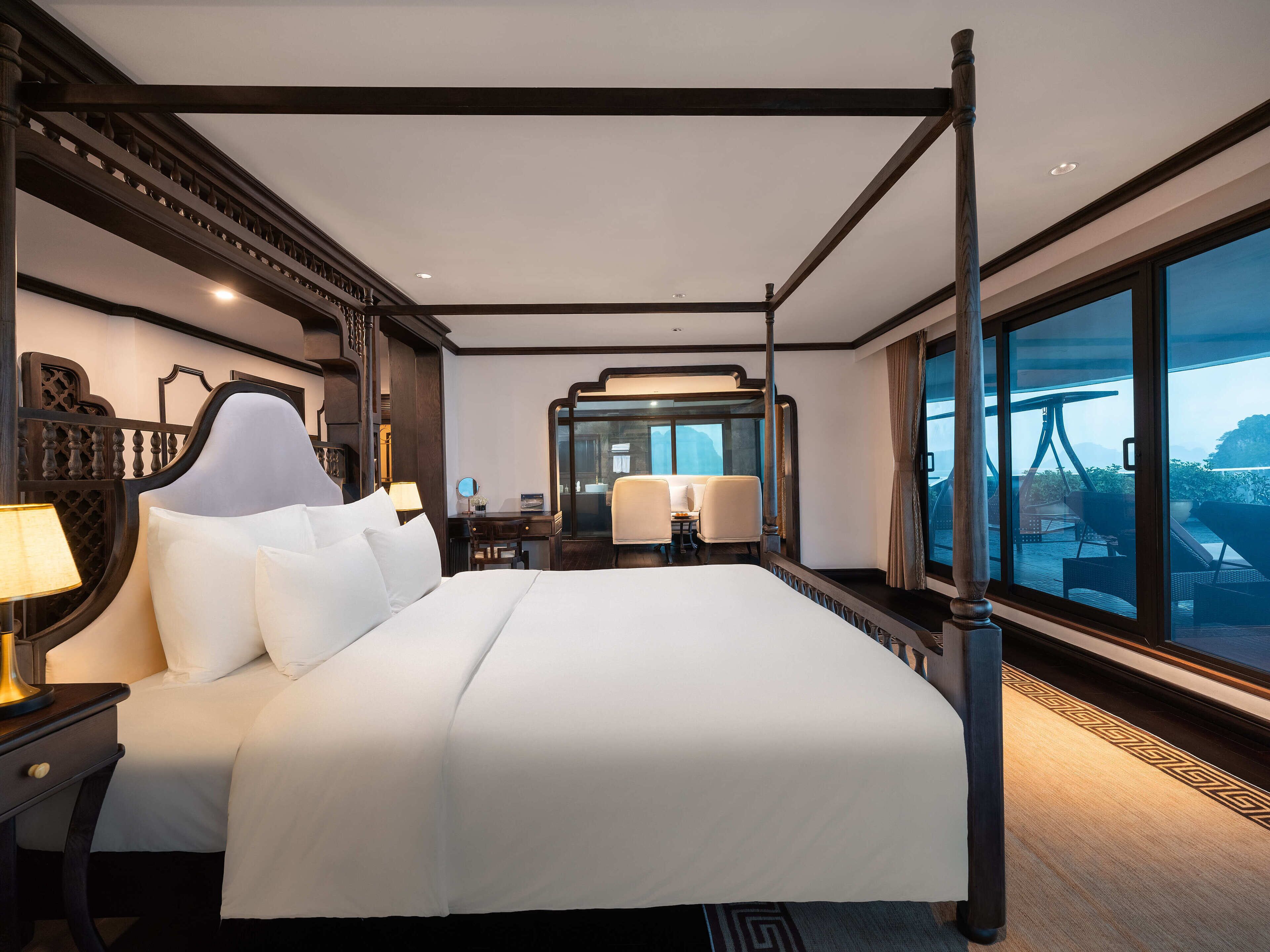 A four-poster bed with a large window, a desk with a chair, and a mirror.