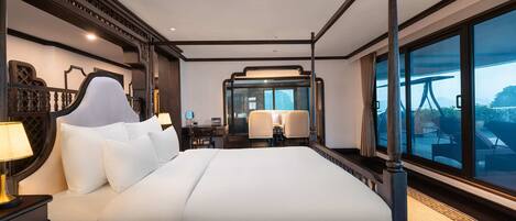 A four-poster bed with a large window, a desk with a chair, and a mirror.