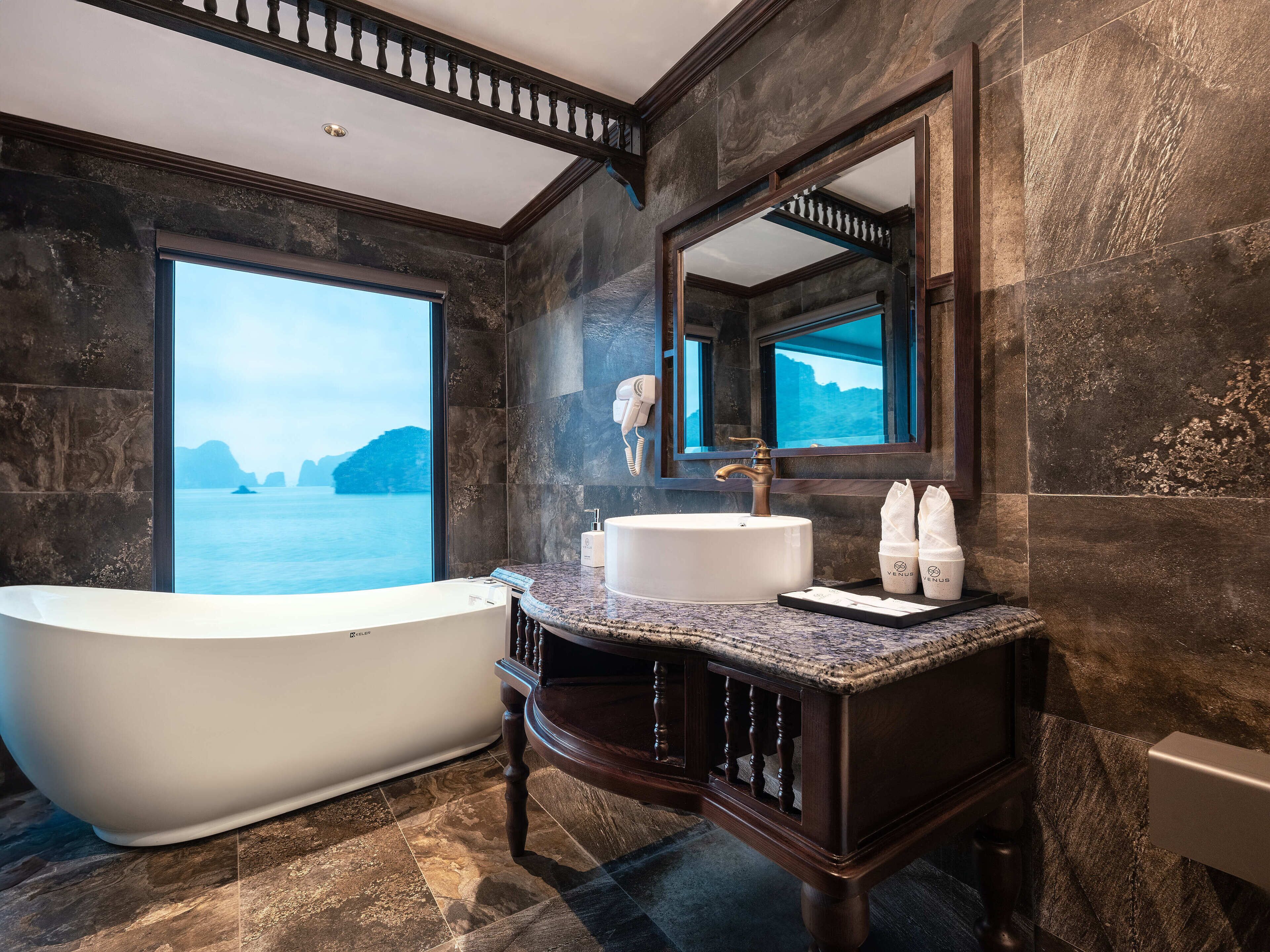 A modern bathroom with a freestanding bathtub, a large mirror, and a view of the sea.