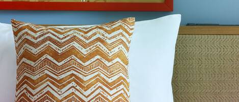 A neatly made bed with a patterned pillow, a wall-mounted lamp, and a framed map.