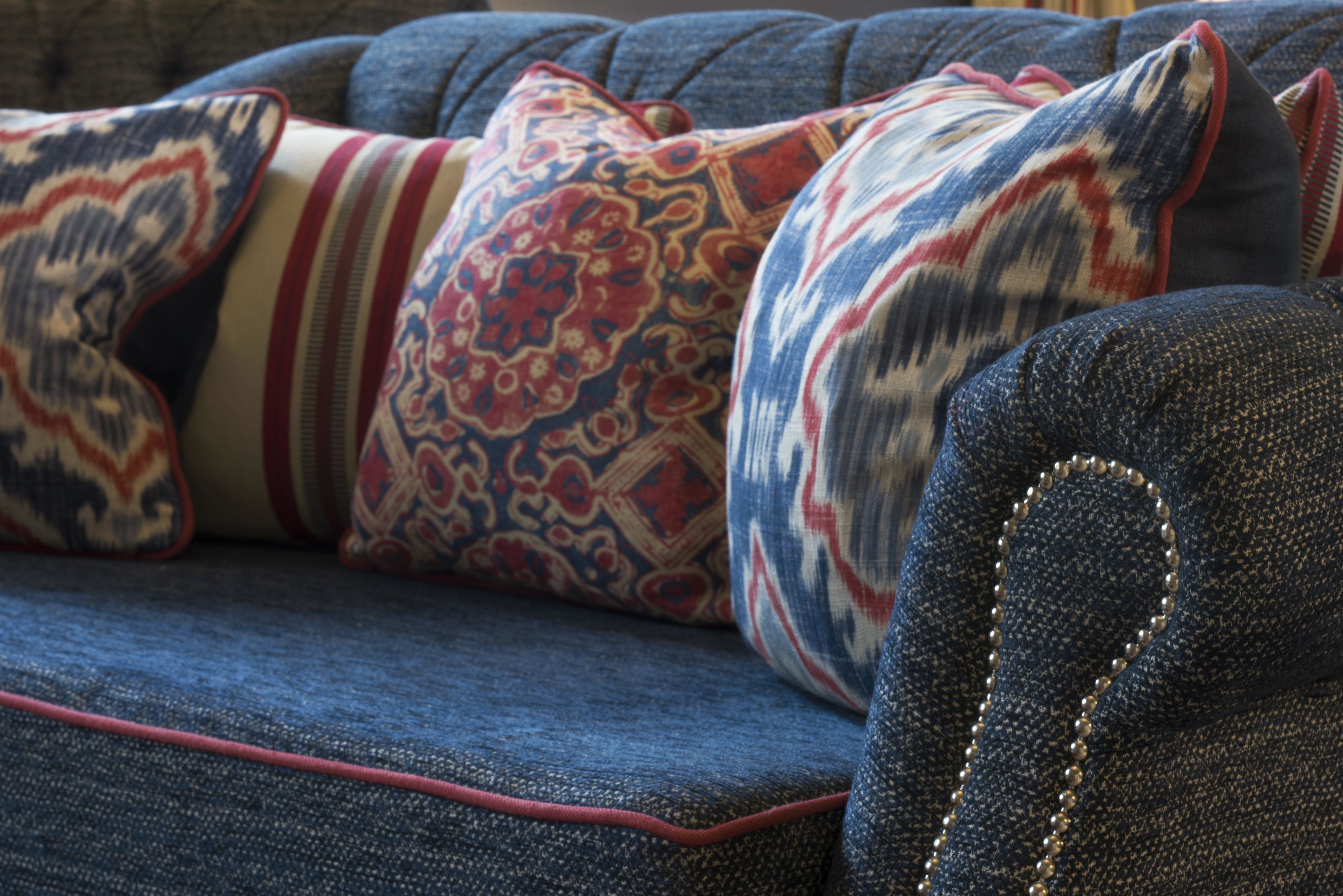 A blue sofa with patterned pillows and a decorative stitch detail.