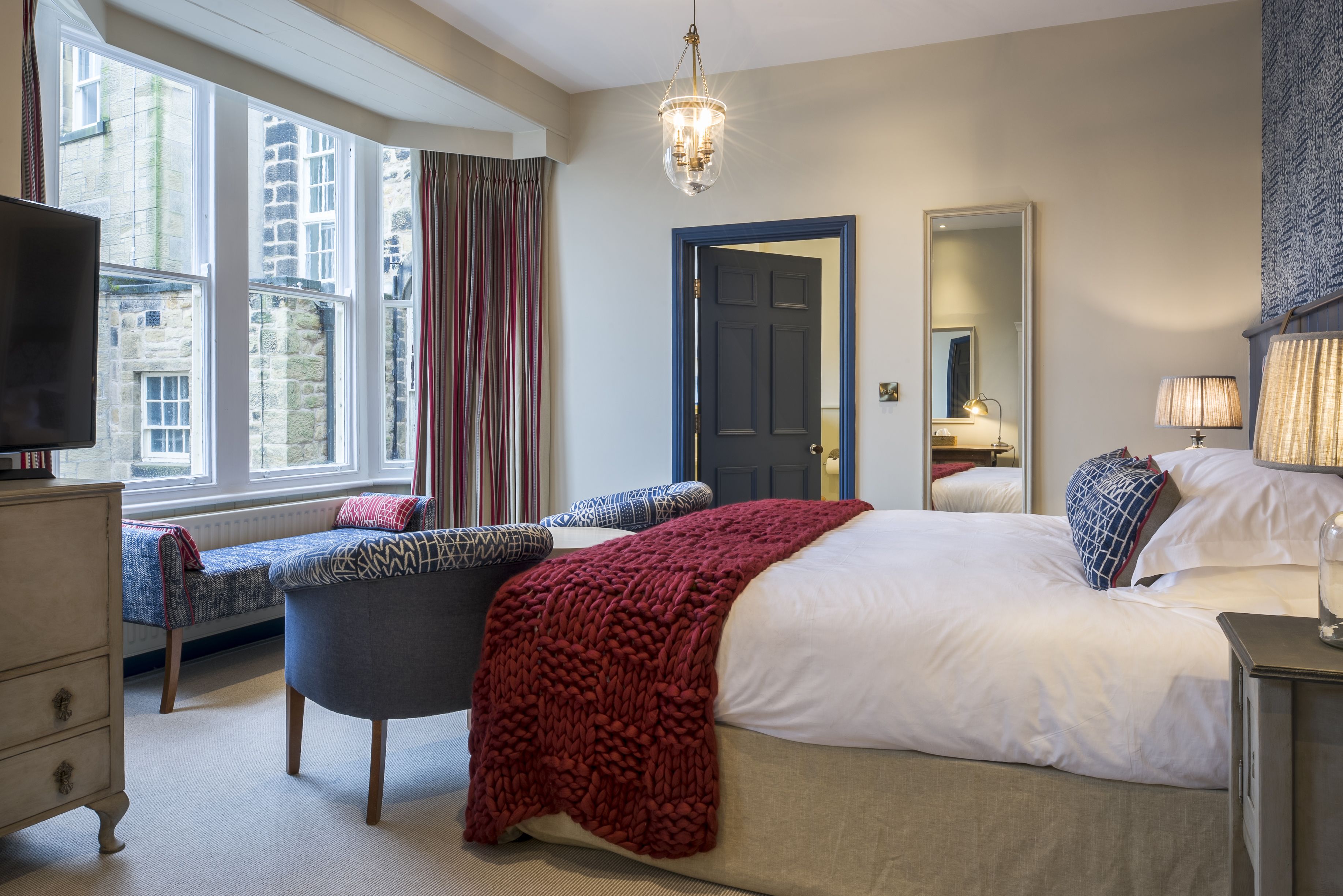 A bedroom with a bed, a bench, a dresser, a television, and a window with curtains.