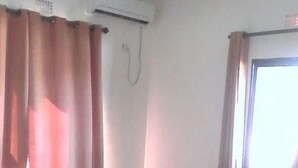 Een hotelkamer met twee bedden, een raam met gordijnen, een airconditioning en een telefoon aan de muur.