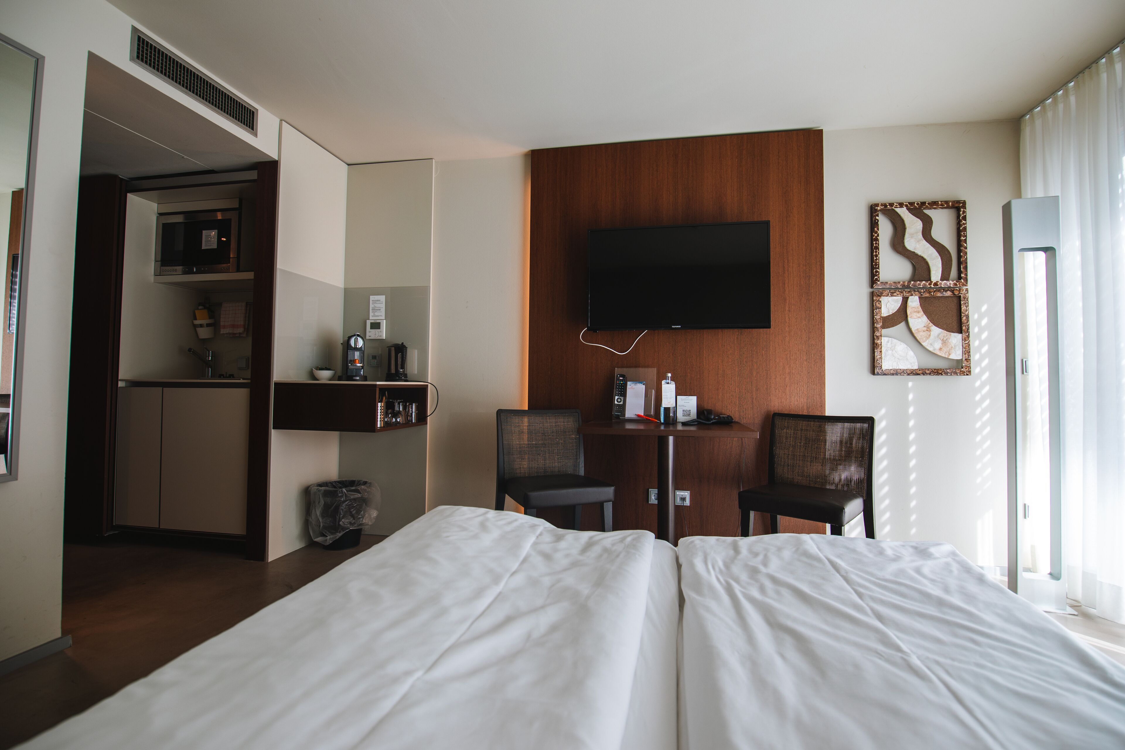 A hotel room with a bed, a desk with chairs, a TV, and a kitchenette.