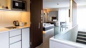 A modern hotel room with a kitchenette, a bed with a headboard, a glass-enclosed staircase, and a large window with curtains. - Car by Side (Heidelberg)