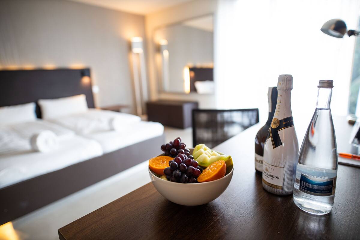 A hotel room with a bed, a bowl of fruit, and two bottles of water on a wooden table.
