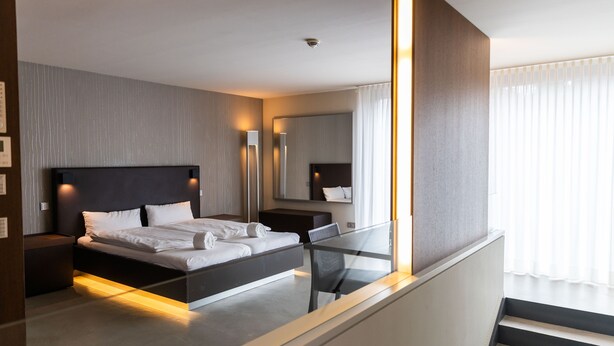 A modern hotel room with a bed, bedside table, and a large mirror. - Car by Side (Heidelberg)