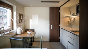 A modern kitchen with a dining area, featuring a wooden table, chairs, a vase with branches, and a view of the city through a window. - Car by Side (Heidelberg)