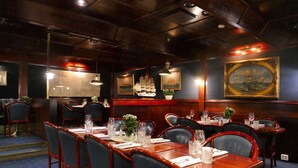 Een restaurant met houten tafels en stoelen, kunstwerken aan de wanden en een vloerbedekking in blauw.