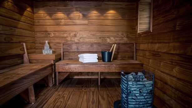 Een houten sauna met banken, een stapel handdoeken, een emmer en een baksteen gevulde container.