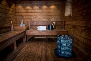 Un sauna en bois, avec des bancs, une pile de serviettes, un seau et un récipient rempli de pierres.