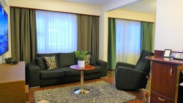 Una sala de estar con un sofá, una mesita redonda con una planta, un televisor y un mueble.