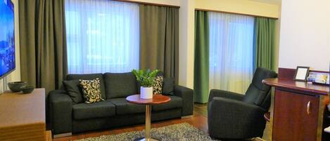 A living room with a sofa, a small round table with a plant, a TV, and a cabinet.