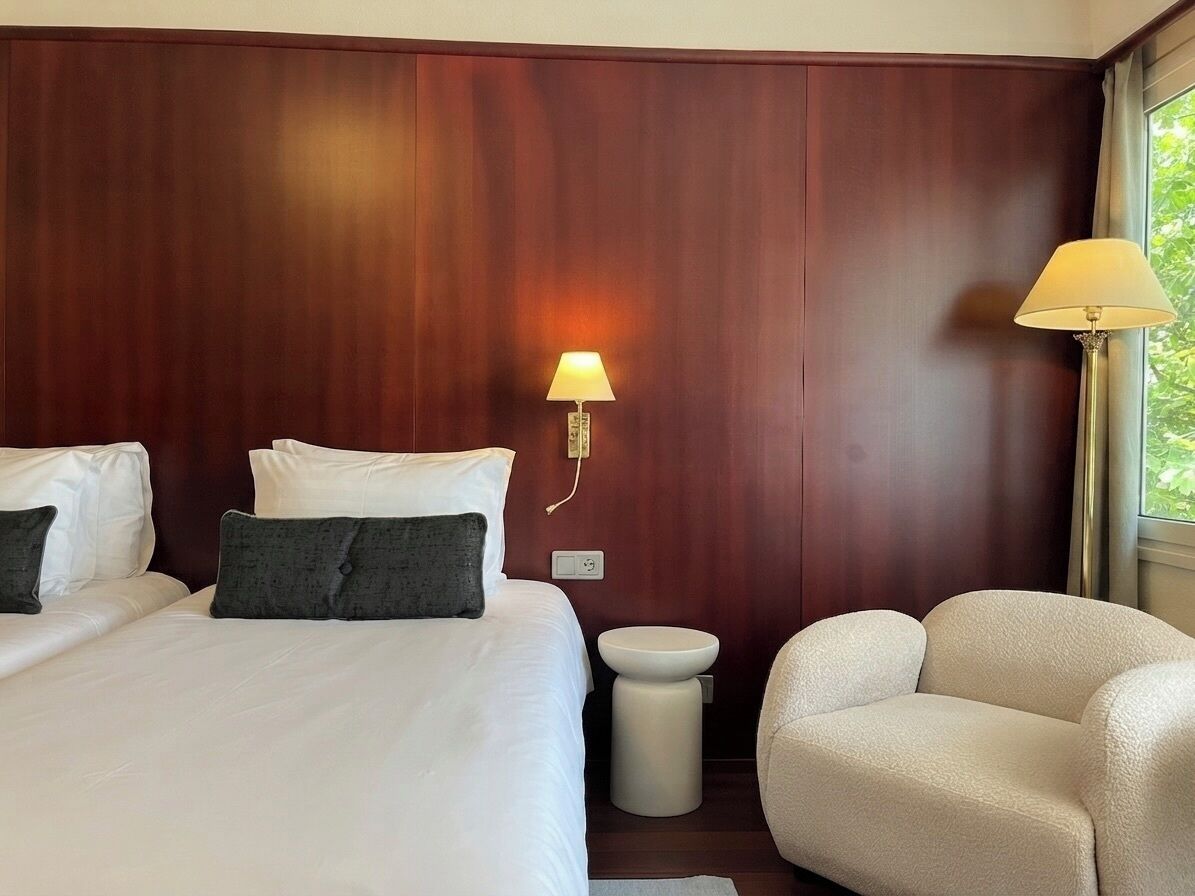 A hotel room with a large bed, a bedside table, a lamp, and a chair.