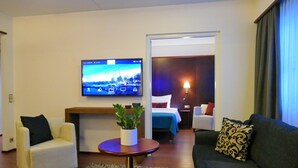 Een hotelkamer met een televisie, een bank, een stoel, een klein tafeltje met een plant, een bed en een nachtkastje.