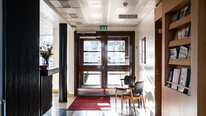 A hotel lobby with a reception desk, a red carpet, a bookshelf with magazines, and a sign indicating directions to the breakfast and restaurant. - Hotel Raumanlinna (Rauma)