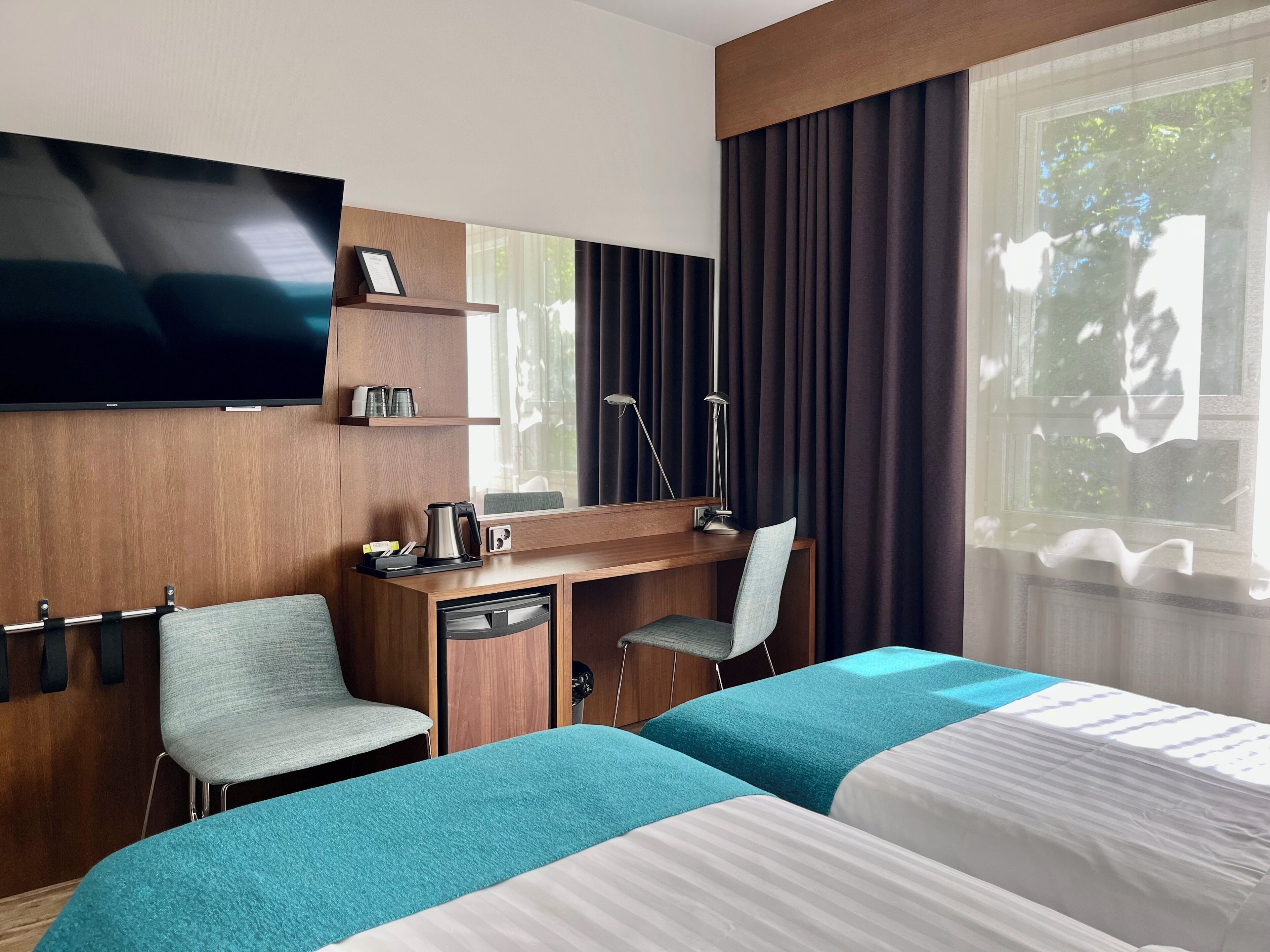 A hotel room with a bed, a desk, a chair, a TV, and a window with curtains.