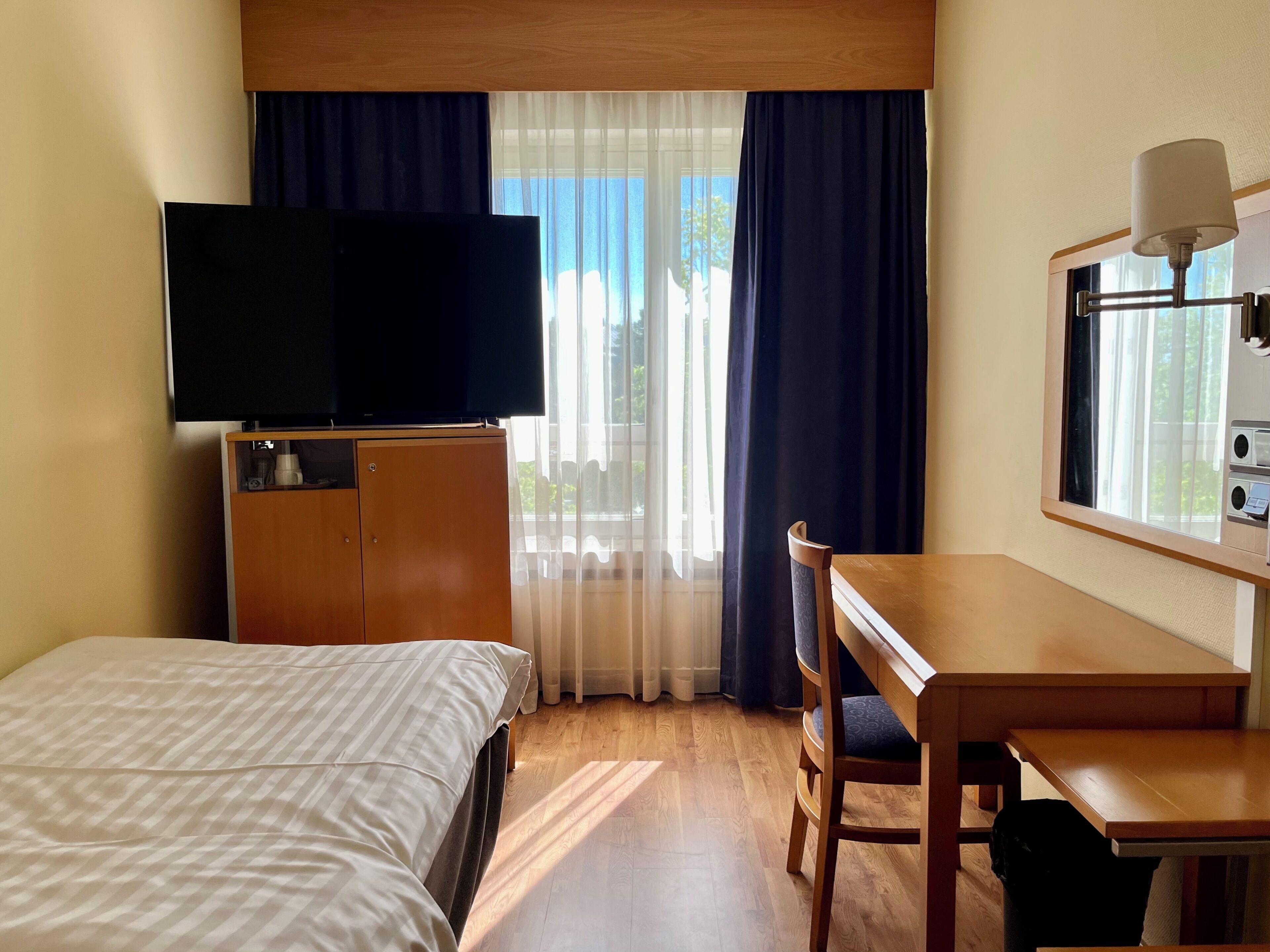 Une chambre d’hôtel avec un lit, un bureau, une télévision et une fenêtre avec des rideaux.
