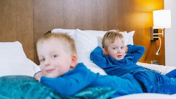 Twee kinderen liggen in bed met witte kussens en een houten hoofdeinde.