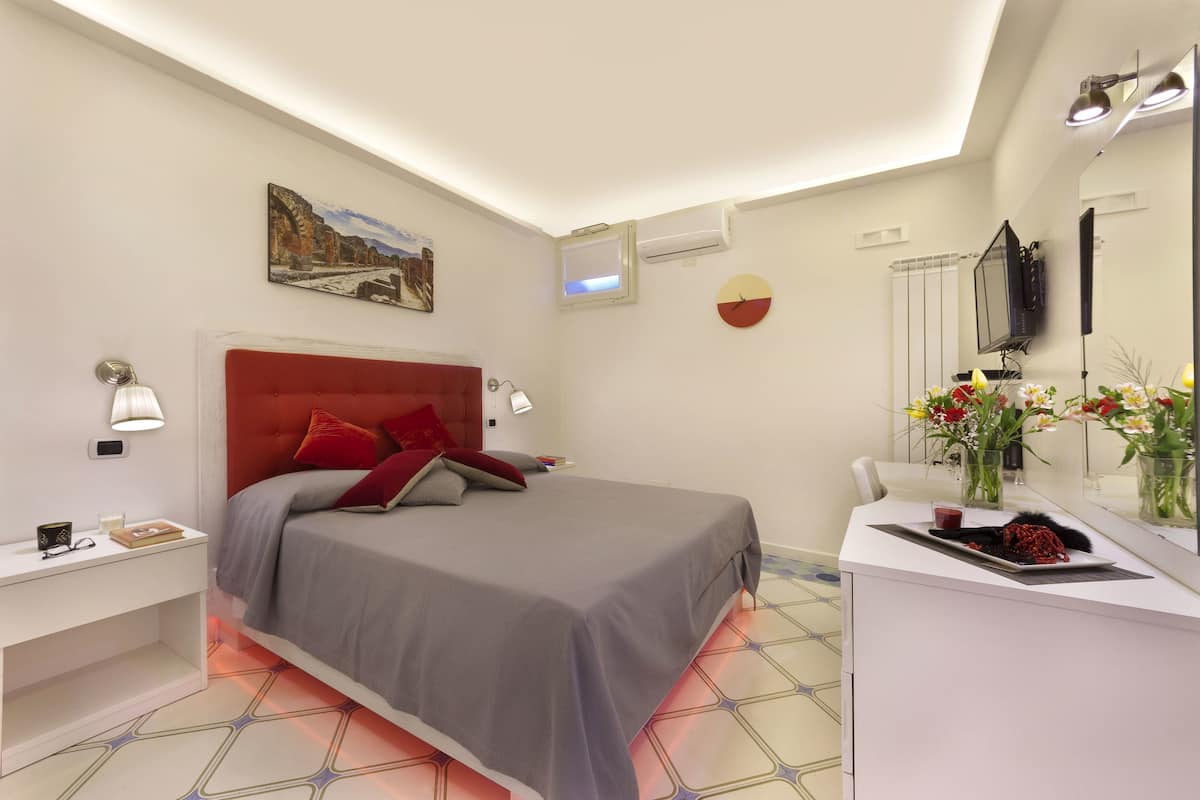 A modern bedroom with a bed, bedside tables, a desk, a mirror, and a painting on the wall.